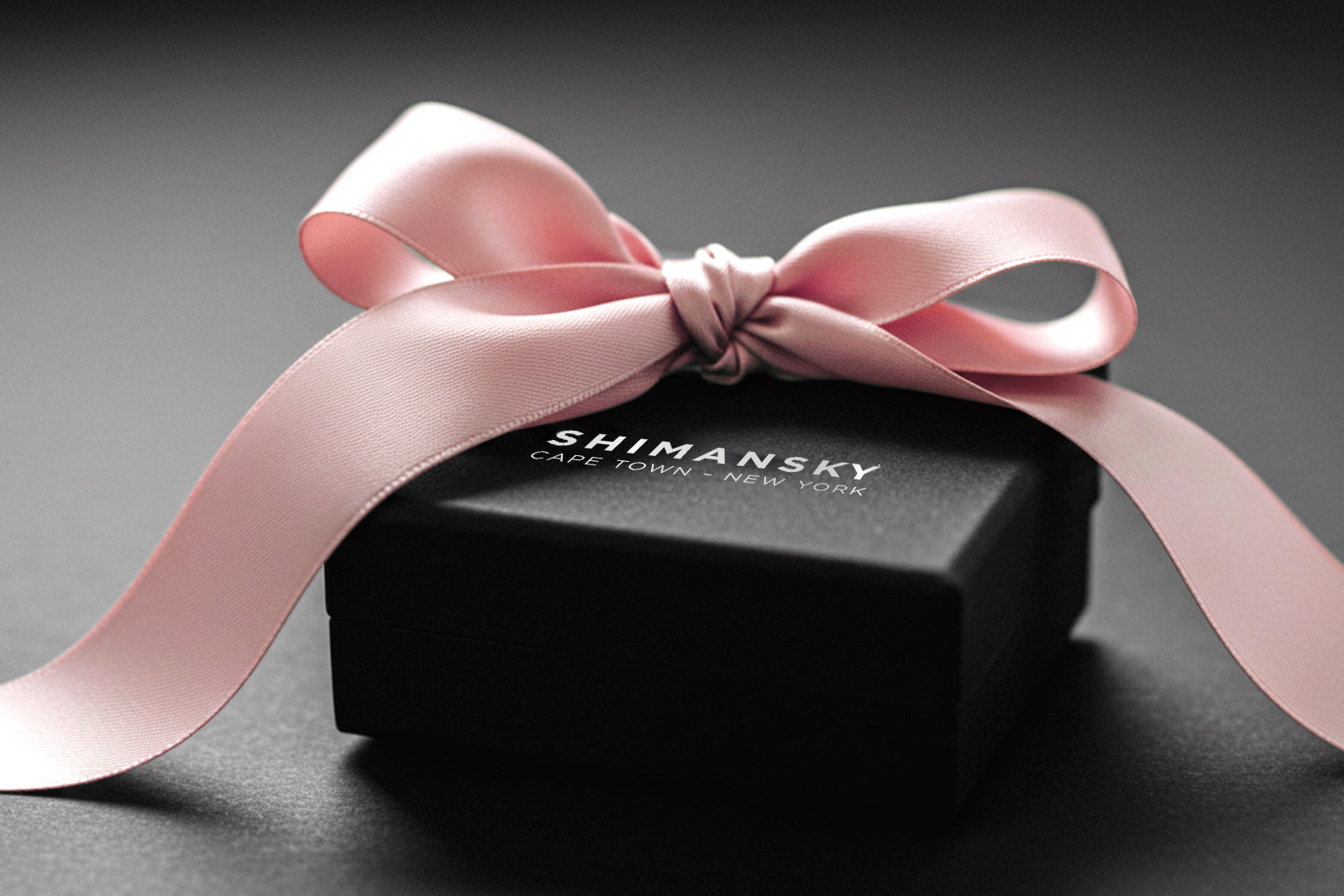 Image showing an elegant Shimansky black jewelry gift box with a beautiful pink bow tied on top. Image courtesy of Shimansky.