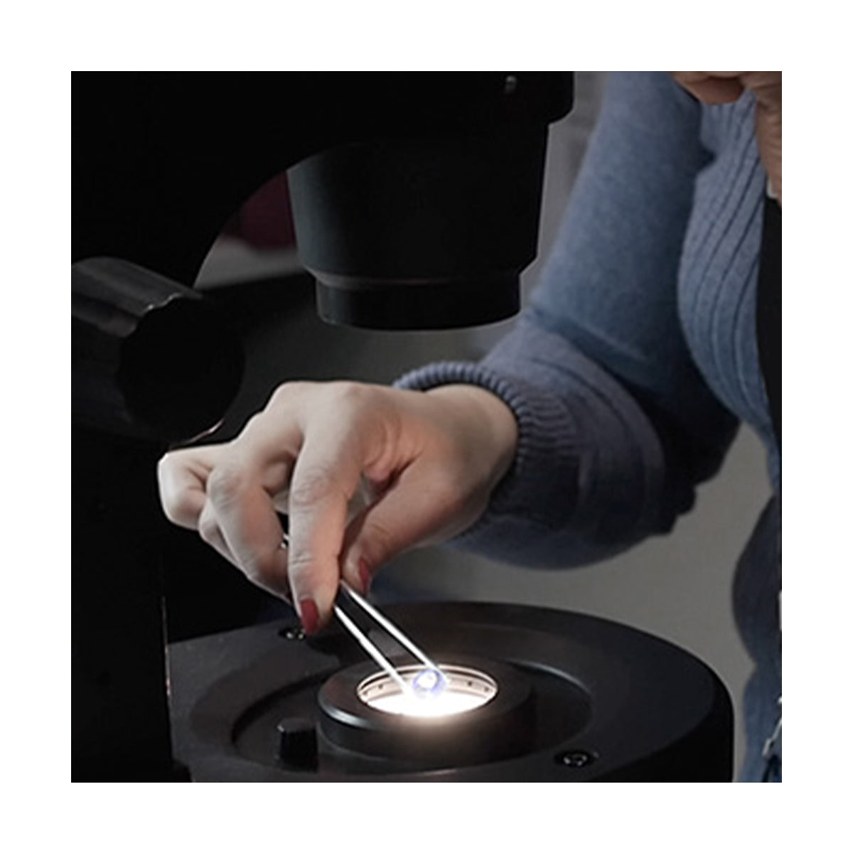 A person peers through a microscope, examining a diamond-encrusted with fascination and curiosity.