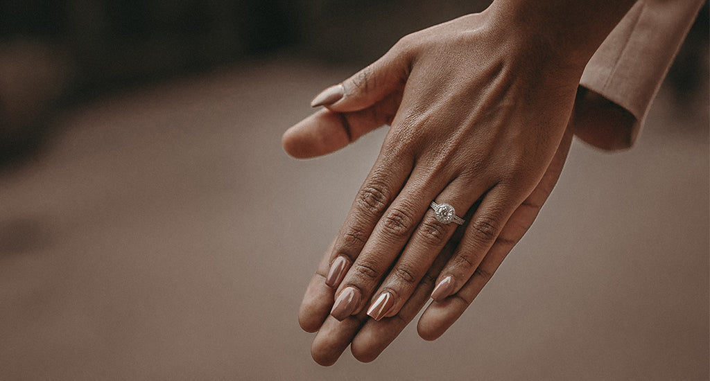 A romantic scene of a couple holding hands with Shimansky Halo Diamond Engagement Ring