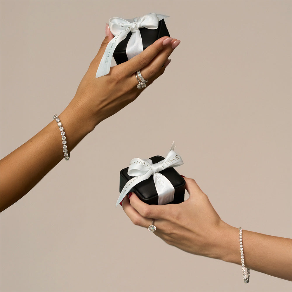 Two hands holding Shimansky Gift Boxes wrapped in white ribbons.