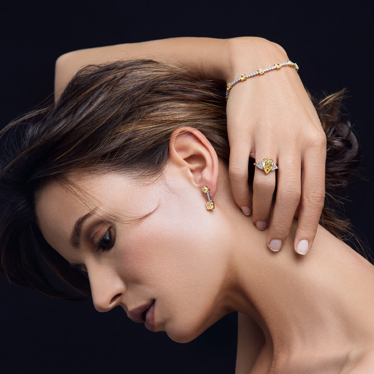 A woman elegantly showcases a stunning gold ring, earring and bracelet adorned with exquisite yellow diamonds by Shimansky.