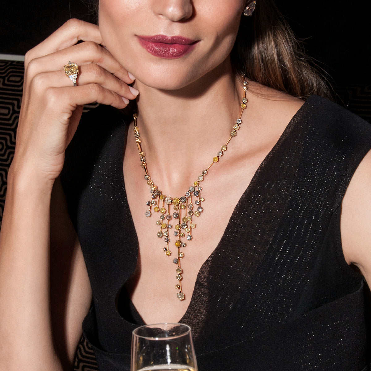 A glamorous woman showcasing a Shimansky yellow diamond necklace, gracefully toasting with a glass of champagne.