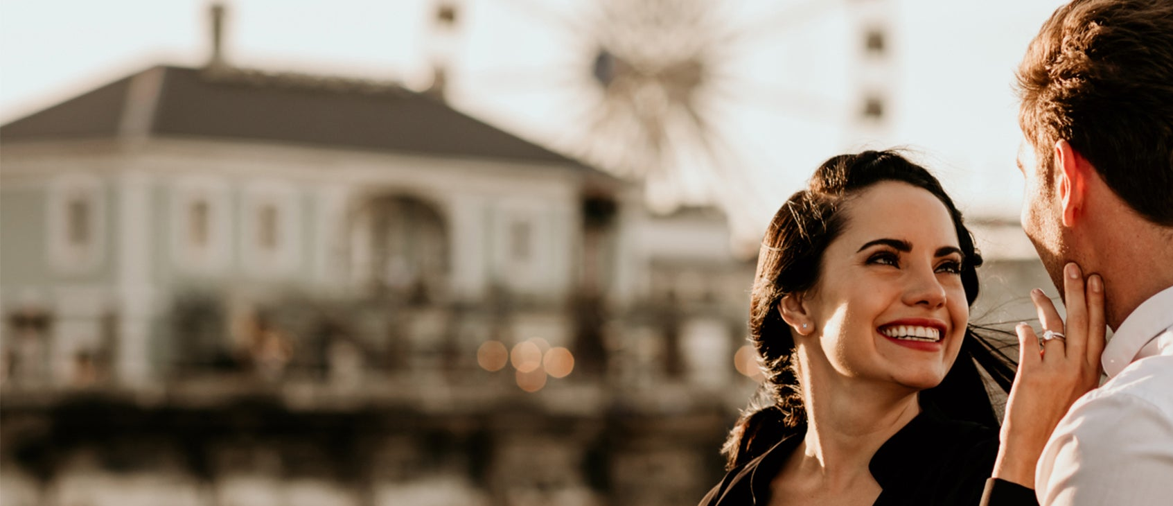 A smiling couple stands before a vibrant ferris wheel, enjoying a delightful moment together at an amusement park.