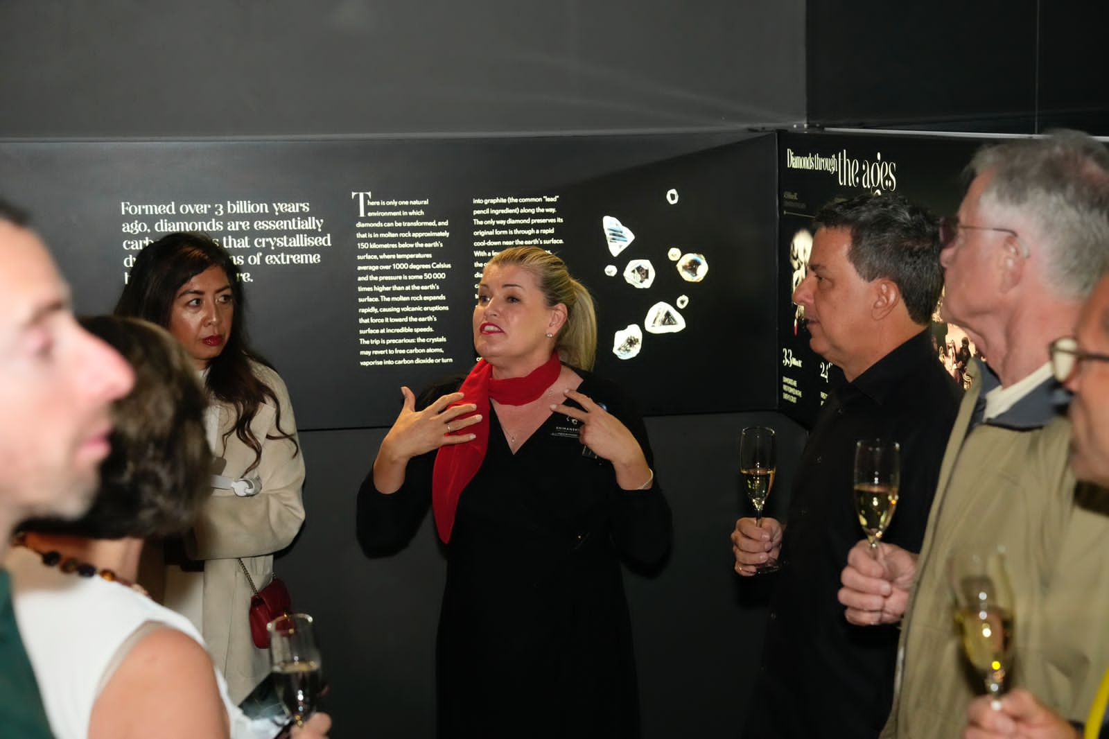 Visitors at the Cape Town Diamond Museum stand around a display, engaging with wine glasses and enjoying the atmosphere.