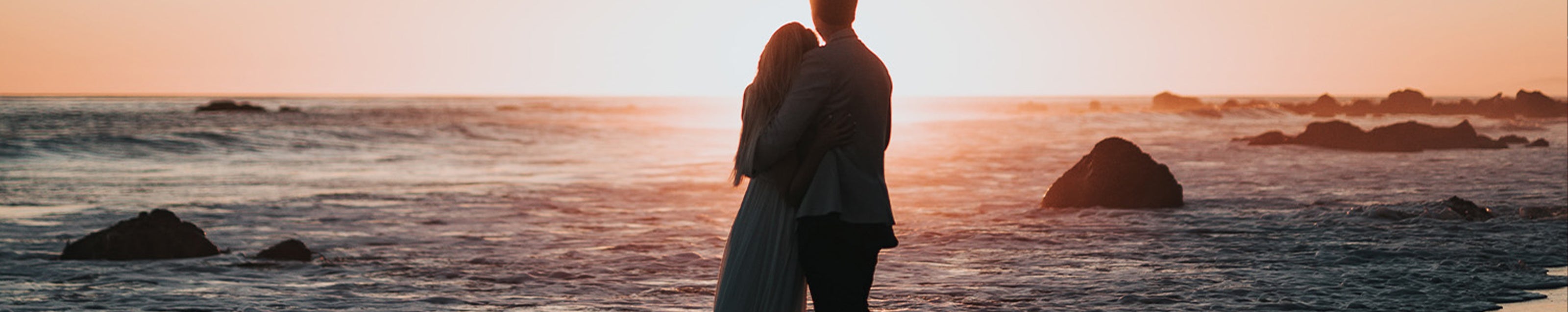 A couple stands on a beach at sunset, embodying romance and adventure in a serene coastal setting