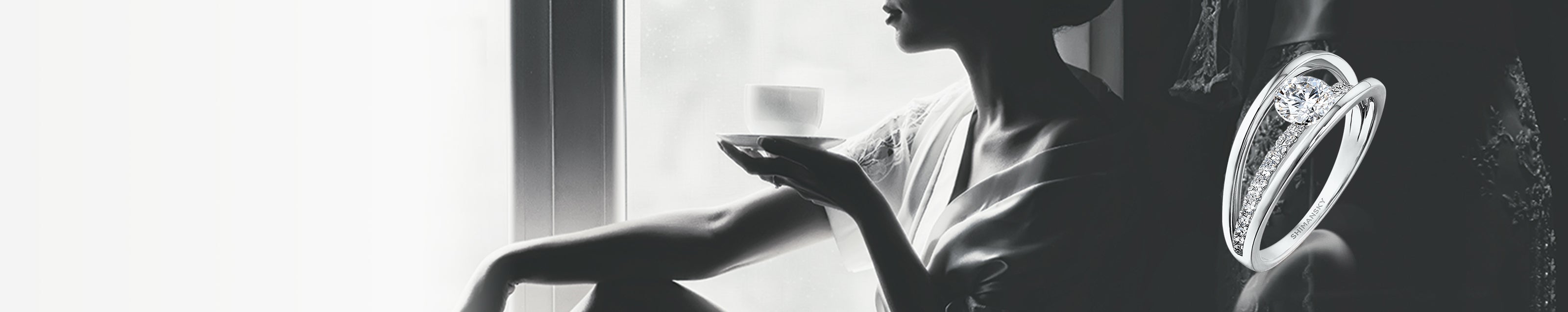 A woman elegantly seated by a window, showcasing her Evolym microset diamond ring by Shimansky, radiating sophistication.