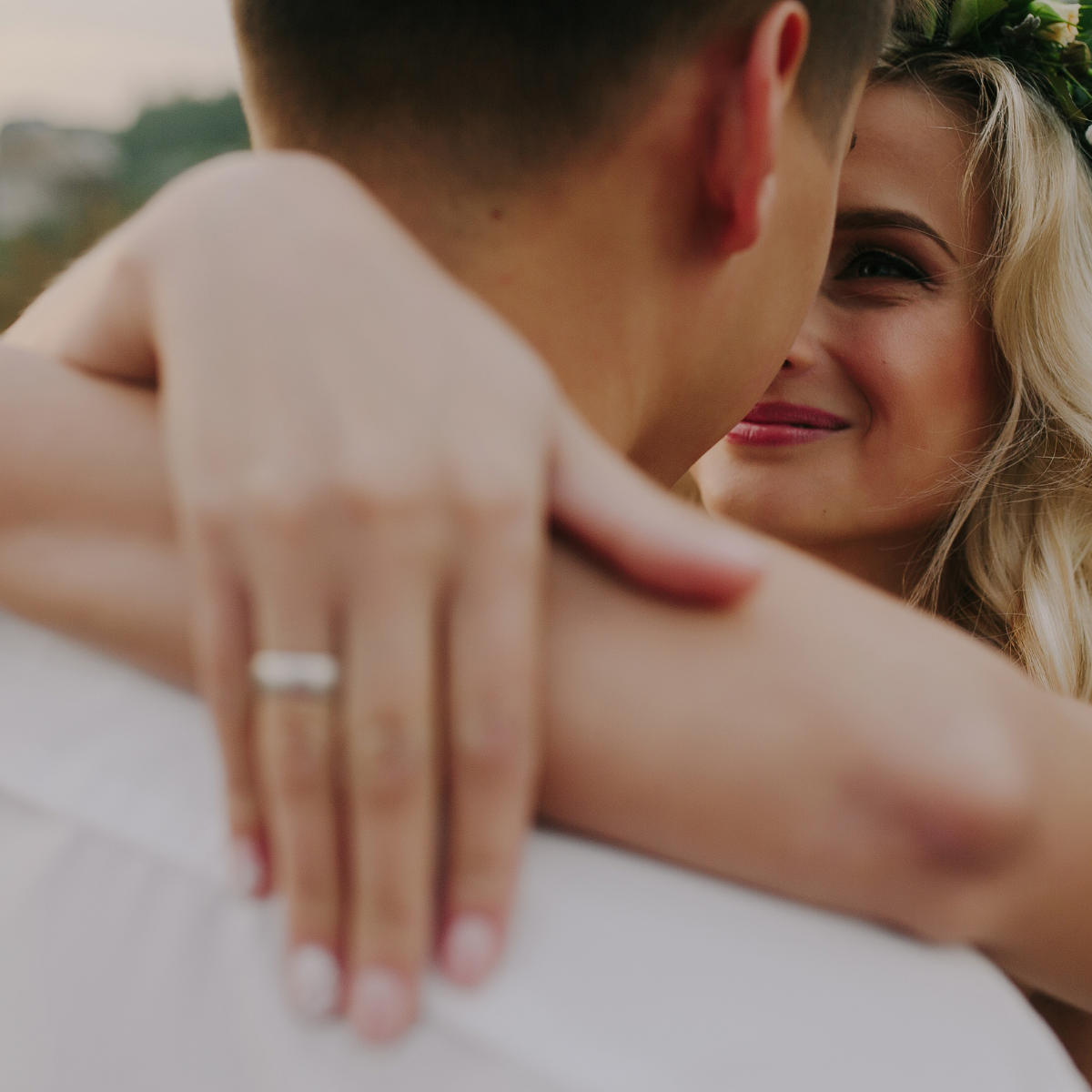 Woman smiling as she embraces her partner, with a Shimansky diamond engagement ring on her hand, resting on his shoulder.