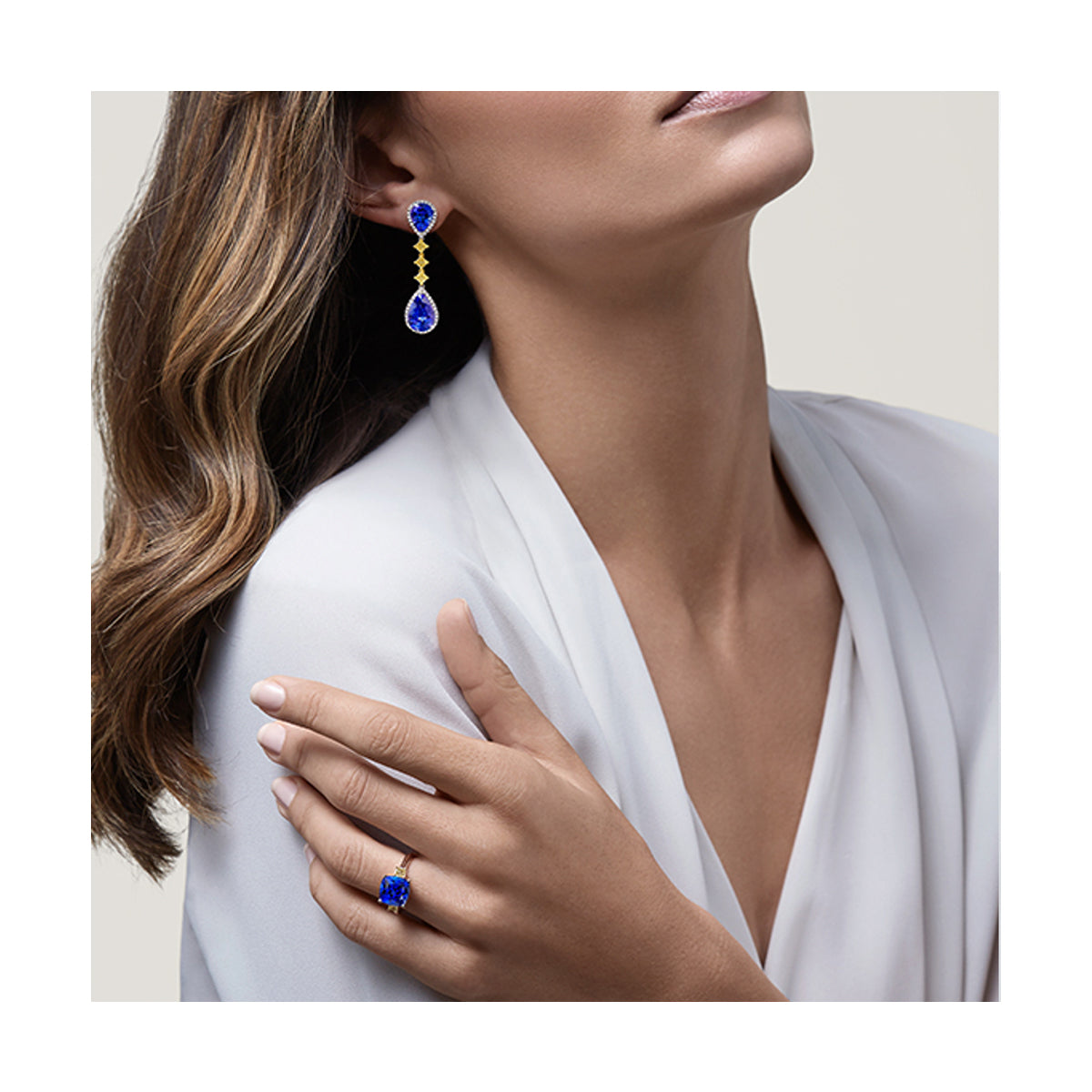 A woman elegantly adorned in a white blouse, complemented by stunning tanzanite blue earrings and ring.