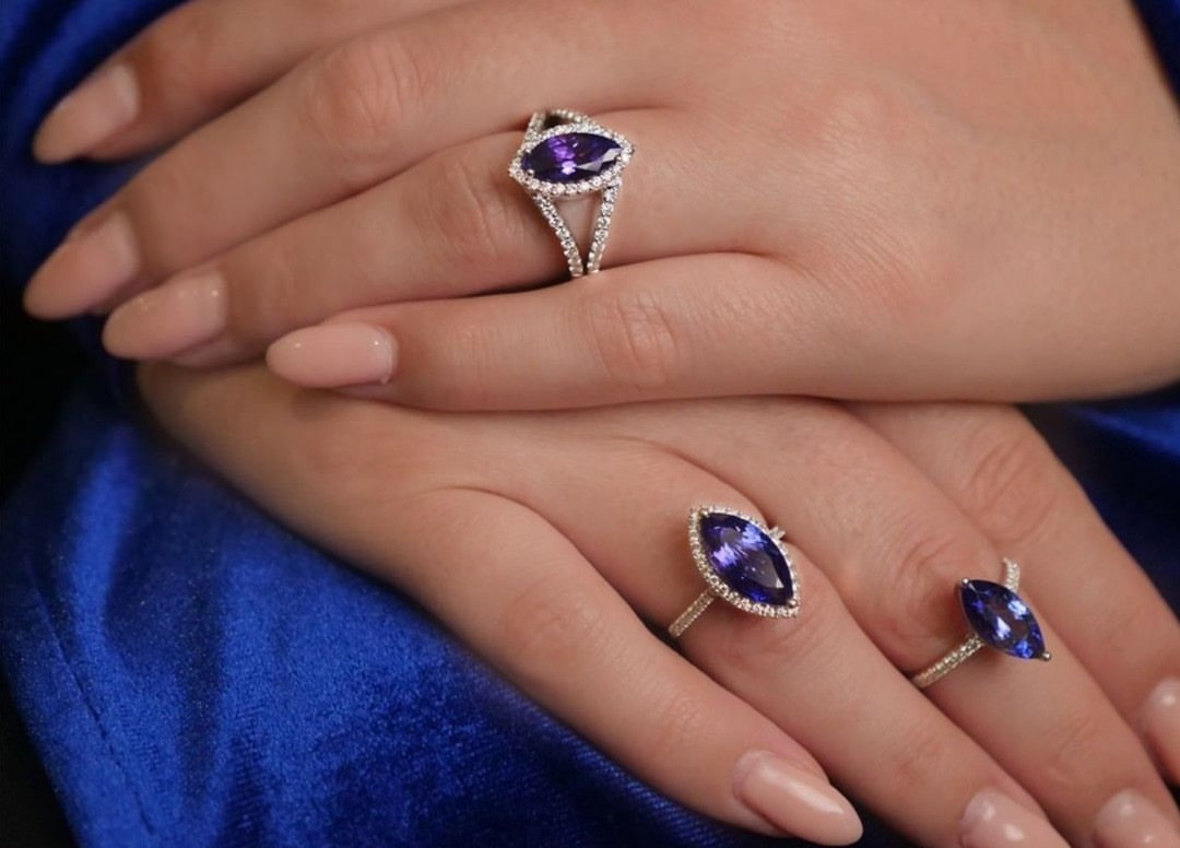 Three Shimansky Tanzanite solitaire rings worn over blue satin, including a pear-shaped ring with a diamond halo and split shank