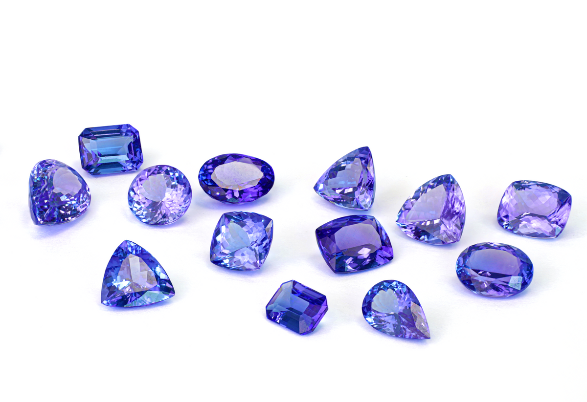 Loose Shimansky violet-blue Tanzanite in round, oval, pear, trillion cuts on a pale background.