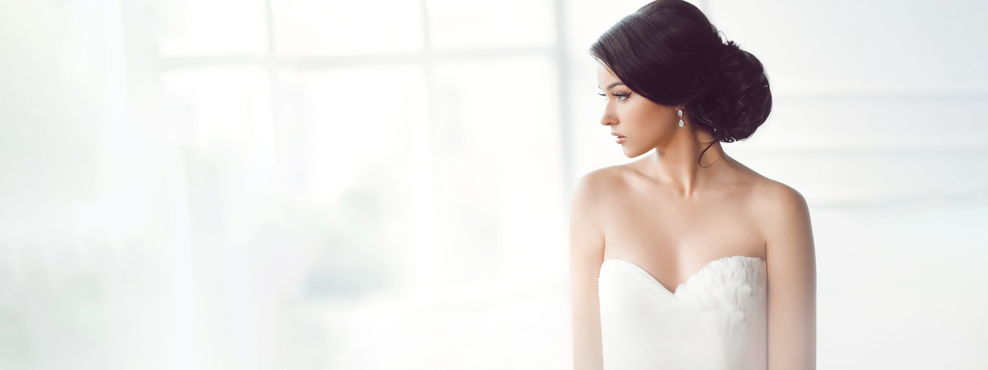 Dressed in a flowing white gown, a woman gazes out the window, embodying grace and tranquillity in a luxurious setting.